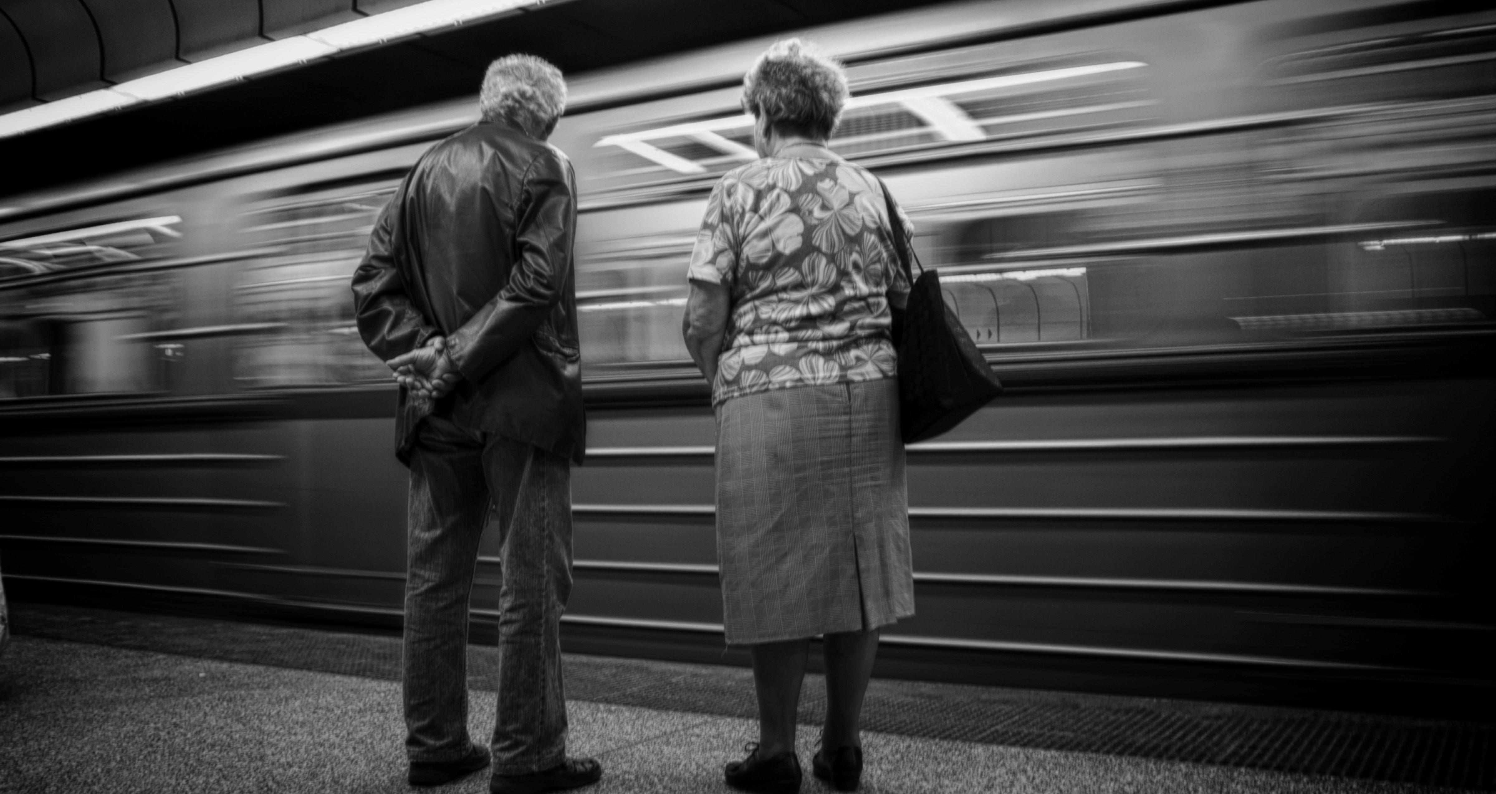 Et eldre par står på en perrong og et tog suser forbi