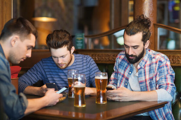 Picture of men drinking beer and preoccupied using their mobile phones