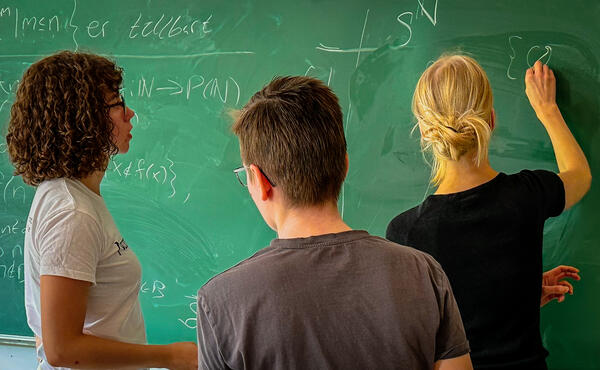 Three students doing mathematics at the blackboard