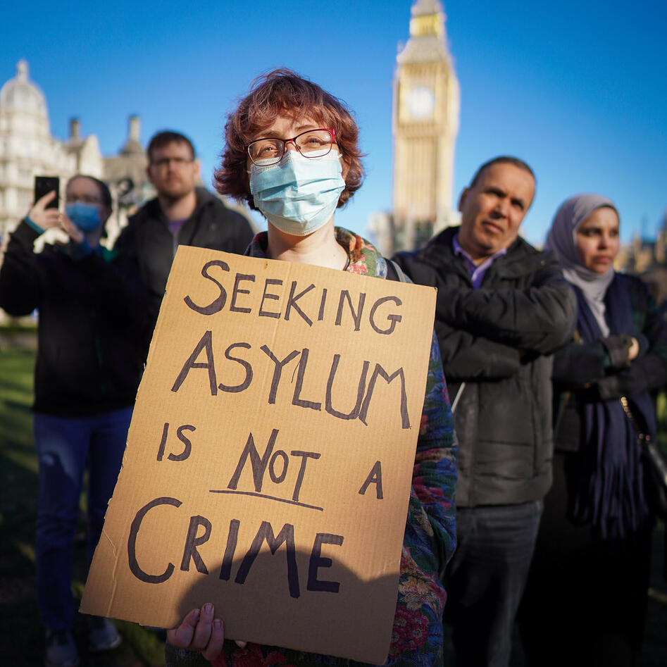 A woman wearing a face-mask with a placard with the words Seeking asylum is not a crime