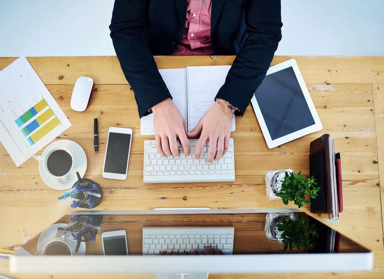 The hands of a man writing on a keyboard on a tidy desk