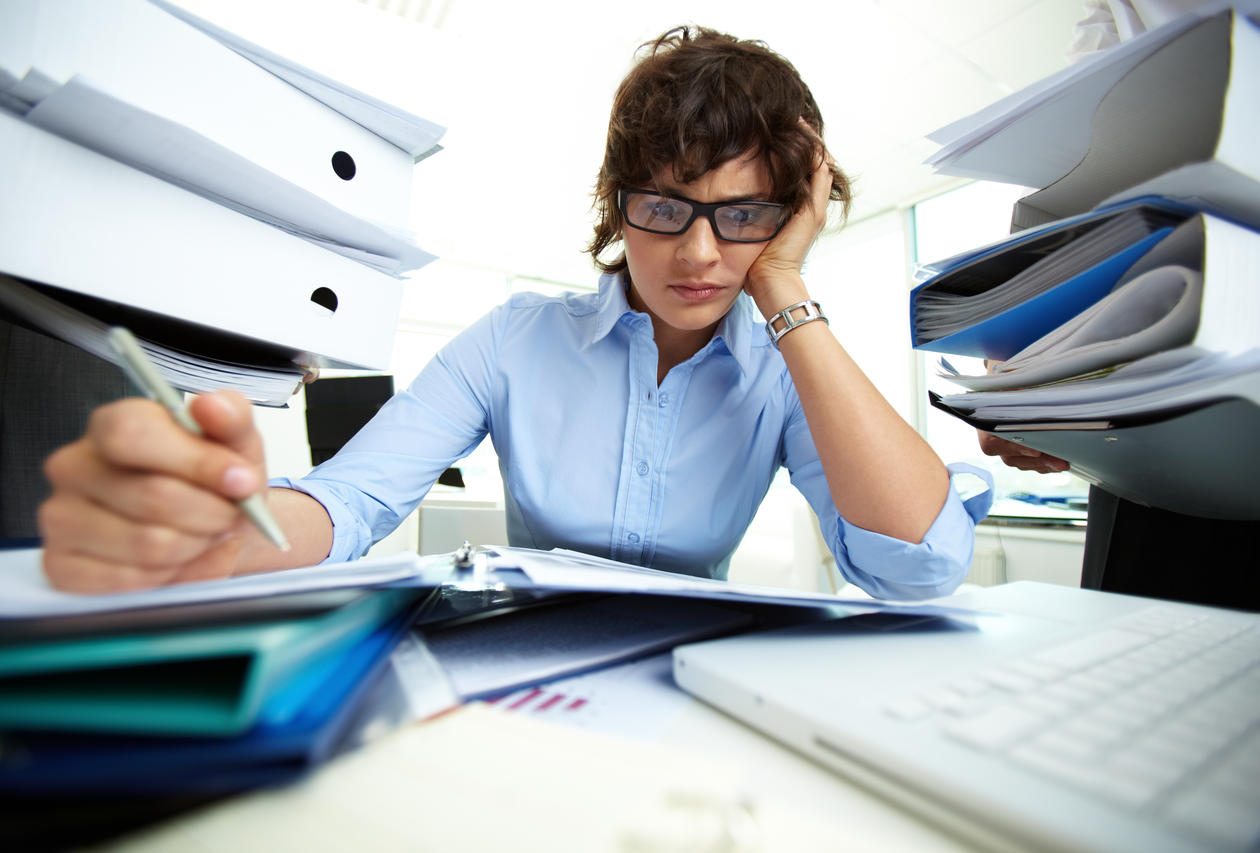 Extremely overworked woman at her desk surrounded by paper work; used to illustrate article about research on work addiction.