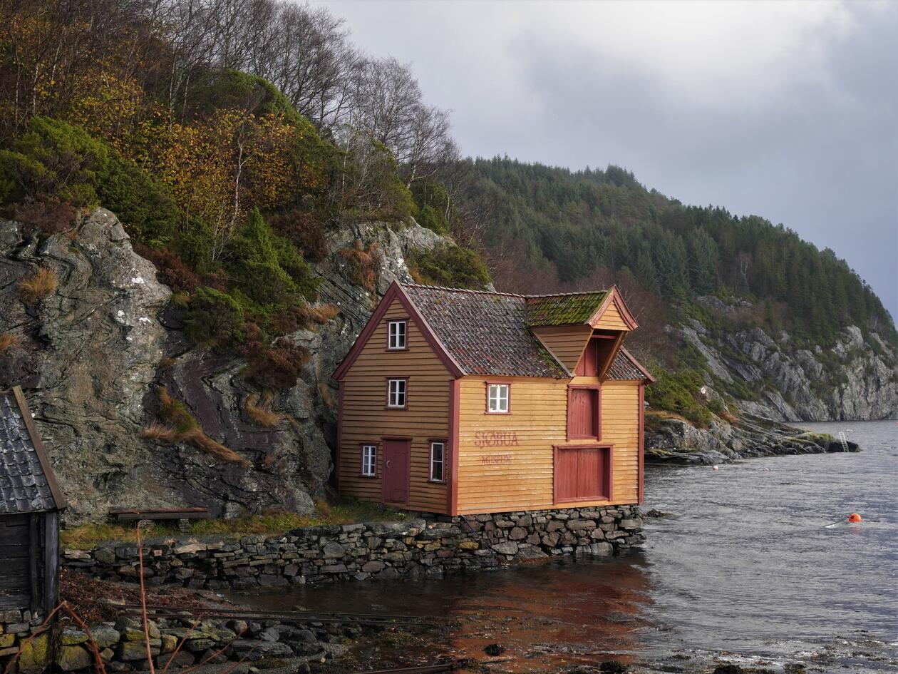 Gammelt båthus/naust i fjæren. Står på en oppmuret kai.