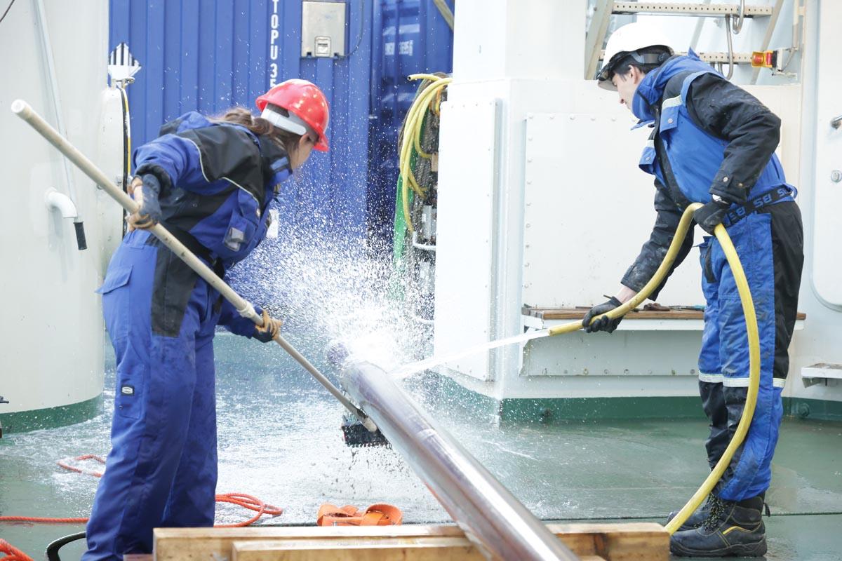 Two people wash and scrub a core sampler on a ships deck