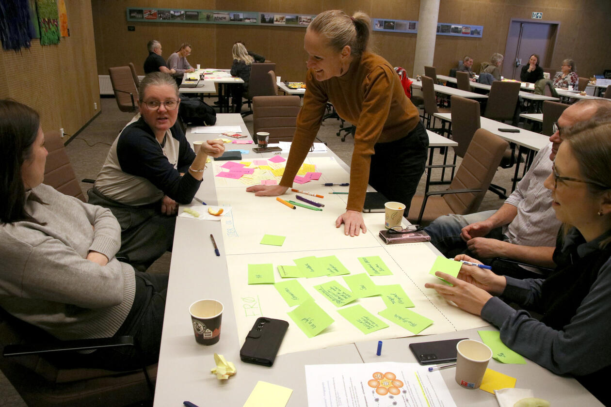 Woman leaning over a tabled which is covered by colourful post-it notes simling towards to women having a discussion