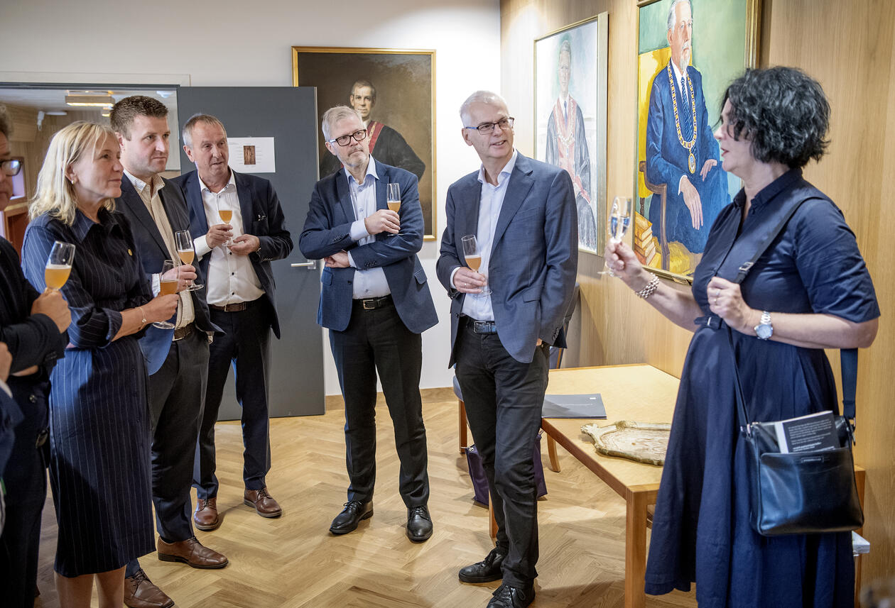 Flere penkledde folk snakker med hverandre og holder hver sine glass