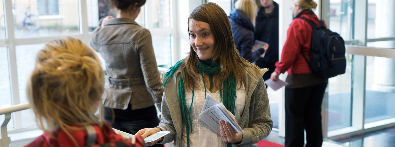 En jente deler ut flyers til studenter i inngangspartiet til SV-bygget