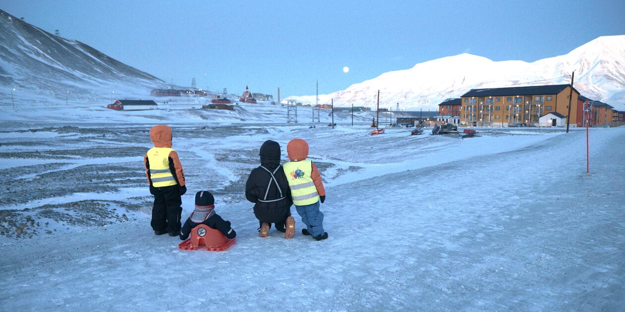 Bilde fra Svalbard med snø og barn som har akebrett, vinterklær og refleksvester