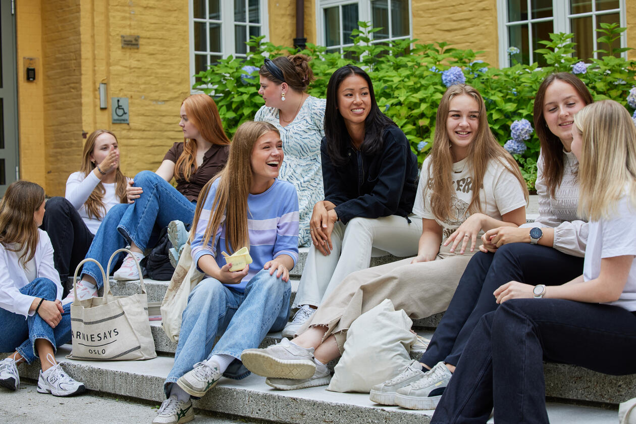 Studenter som sitter på en trapp og snakker sammen. De er glade.