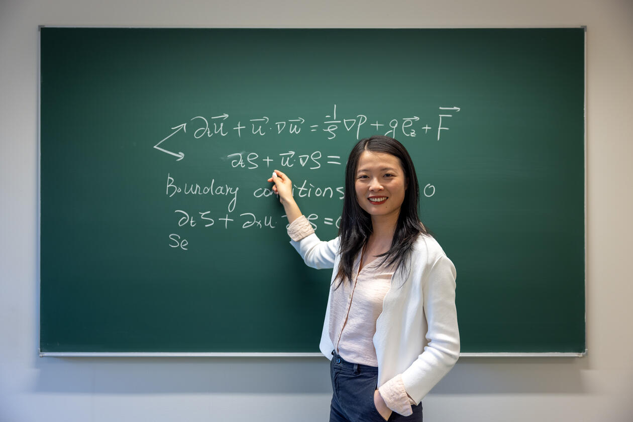 Yan Li in front of a chalk-written equation on the blackboard.