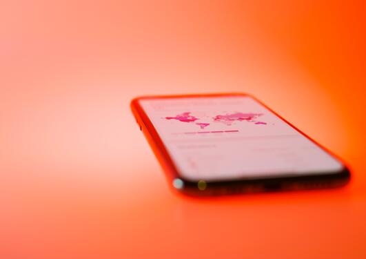 Photo of a mobile phone on a red background, indicating infection rates for the COVID-19 pandemic.