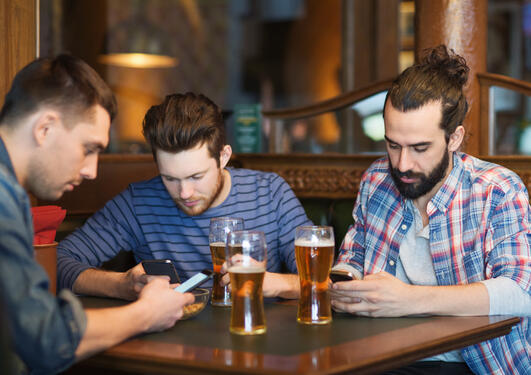 Picture of men drinking beer and preoccupied using their mobile phones