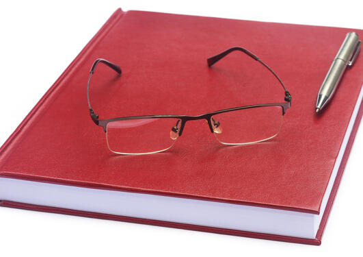 Illustrasjonsbilde rød notatbok med briller og en penn liggende oppå