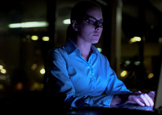 Kvinne sitter i et mørkt rom foran pc og arbeider