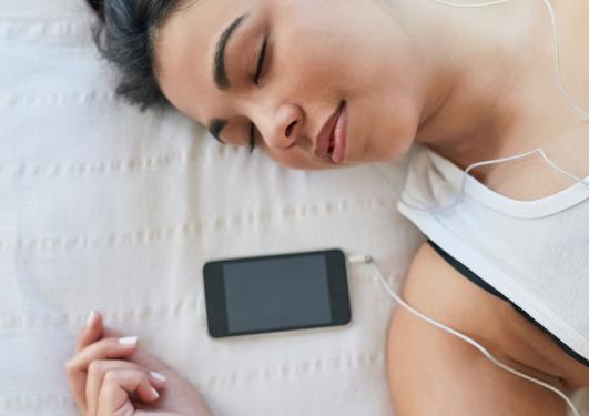 Woman relaxing in bed listening on her phone