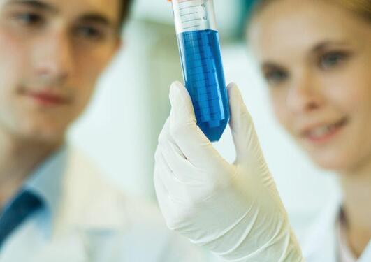 Image of two persons in lab coats holding a glass vial with a blue solution