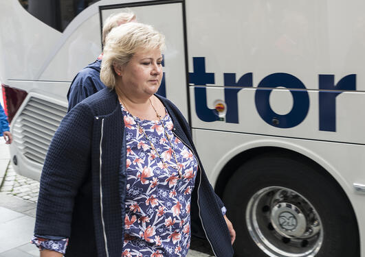 Erna Solberg gående langs en buss der teksten "tror" er synlig
