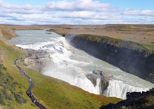 Gigantic waterfall at Iceland, and people walking into a view plateau in the middle of it.