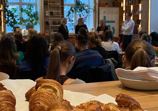 A picture of a panel conversation with a view to the stage. People sitting and listening, croissants closest to the camera as a focal point.