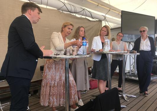 A passionate Kristin H. Holth speaking during a debate in Arendal, Norway on 14 August 2019  whilst (left to right) Inga Berre, Hege Økland, Ragnhild Freng Dale, and Hege Hammersland-White listen. Moderator Ole Øvretveit on far left. 