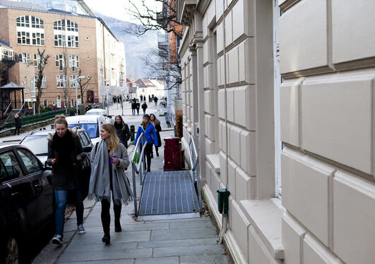 Studenter i vinterklær går i gaten utenfor Sosiologisk institutt, med SV-bygget og Ulriken i bakgrunnen.