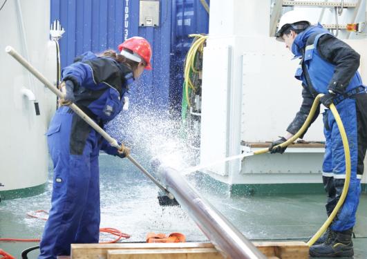 Two people wash and scrub a core sampler on a ships deck