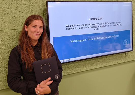 Lisa Aaslestad foran en skjerm med presentasjon av masteroppgaven hennes.