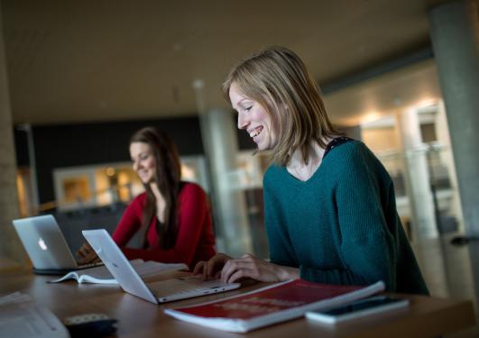 Ung kvinne sitter og smiler foran pc