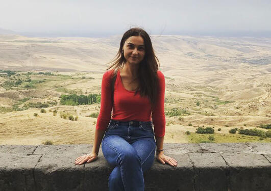 Olga sitting on a wall with landscape in background.