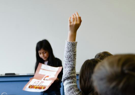 Jente rekker opp hånden i klasserom